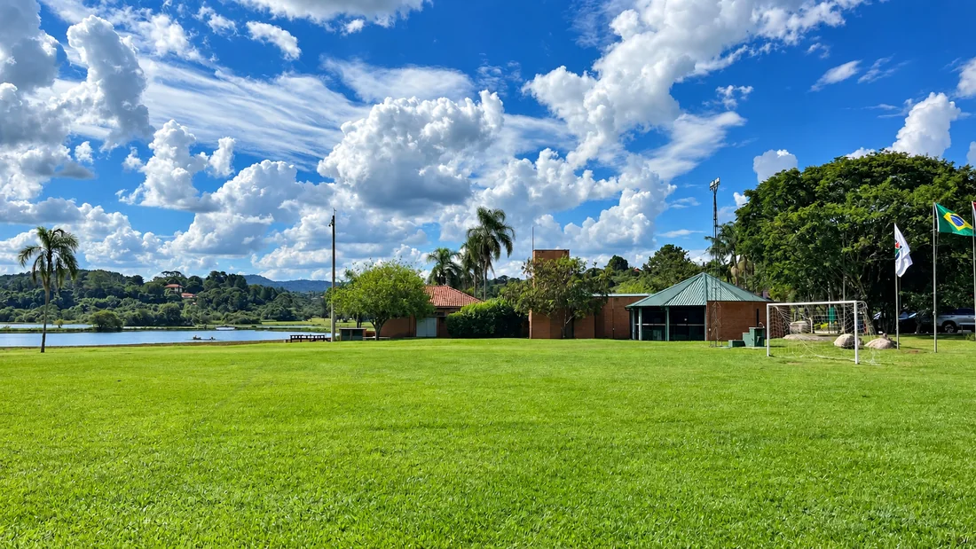 Campo gramado do Patrimônio do Carmo cercado de árvores, junto ao lago